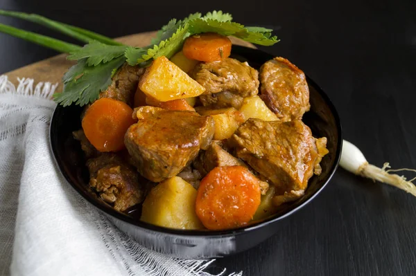 Patates, havuç ve siyah arka plan w üzerinde otlar ile sığır eti güveç