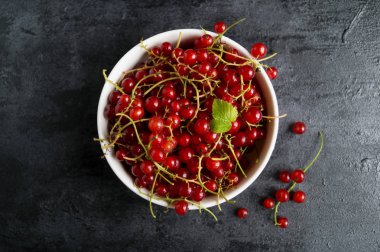 Siyah masada beyaz bir kase kırmızı kuş üzümü.
