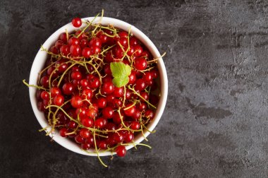 Siyah masada beyaz bir kase kırmızı kuş üzümü.
