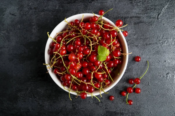 Siyah masada beyaz bir kase kırmızı kuş üzümü.