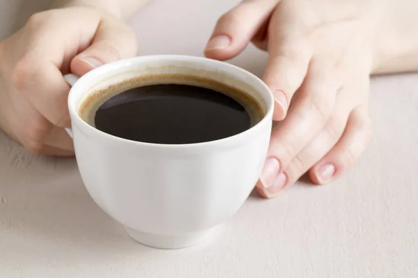 Руки, держащие чашку кофе на светлом столе . — стоковое фото