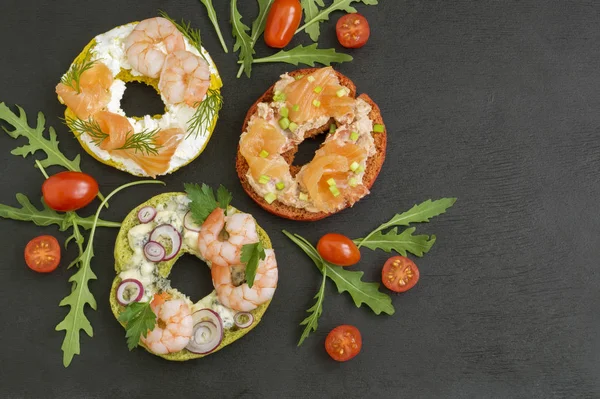 Bagels with cream cheese, salmon, shrimp. On a black background. — Stock Photo, Image