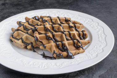Çikolata soslu Belçika çikolatalı waffle 'ı. Beyaz bir tabakta.