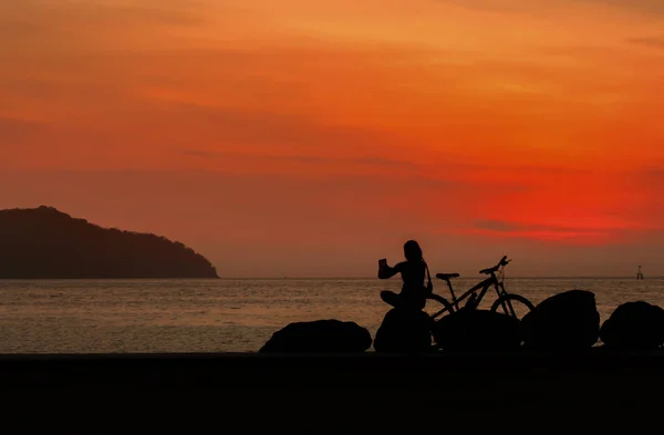 Young lady sitting on the rock with bicycle on a sea coast and e — Stock Photo, Image