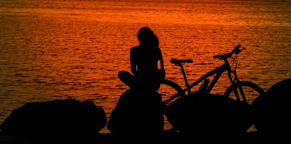 Young lady sitting on the rock with bicycle on a sea coast and e — Stock Photo, Image