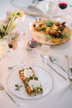 Çiçekli bir tatil masası, yumurtalı bir sandviç, kırmızı balık ve şarap, mumlu.