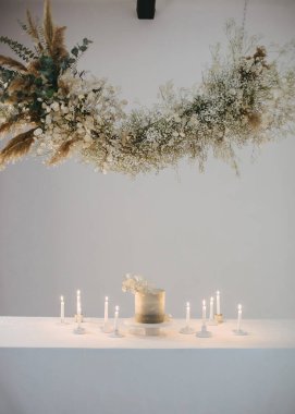 Kurumuş otlardan, yapraklardan, çiçeklerden ve dikenlerden oluşan bir çelenk ve mumlarla dolu bir masanın üzerinde duran bir kaidedeki düğün pastası.