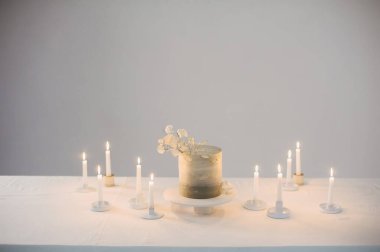 Deadwood filizi ile süslenmiş bir kaidedeki düğün pastası, mumlarla dolu bir masanın üzerinde duruyor. 