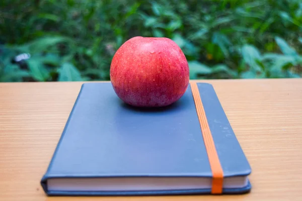 Roter Apfel auf einem Buch mit grünem Hintergrund — Stockfoto