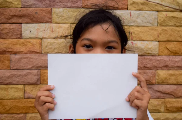 Tyttö pitää valkoinen tyhjä paperi kiviseinälle — kuvapankkivalokuva