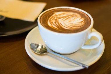 Tahta arka planda beyaz bir fincanda kalp desenli bir fincan kahve.