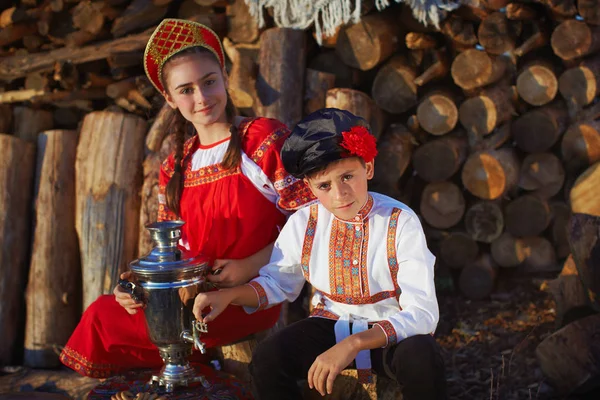 Сестра и брат в русских народных костюмах сидят рядом с Самоваром — стоковое фото