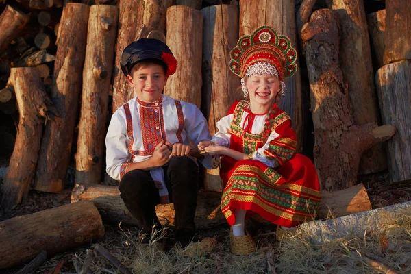 Два русских ребенка в русском народном костюме мальчик и девочка играют вместе и эмоционально улыбаются — стоковое фото