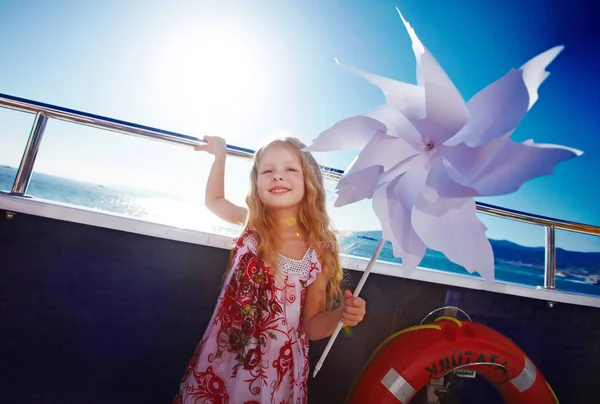 Linda rubia de pelo largo de seis años de edad, chica está jugando con el molinete en la cubierta del barco de crucero, tiempo ventoso — Foto de Stock