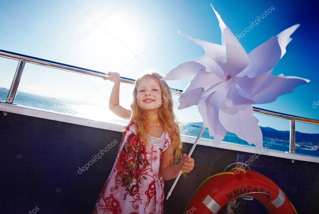 Cute blonde long haired six years old girl is playing with pinwheel on cruise ship deck, windy weather