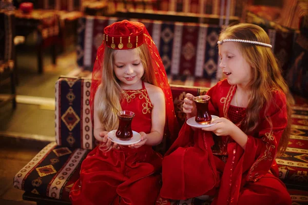 Two girls in folk Arabic costumes drinking Turkish tea together — Stock Photo, Image