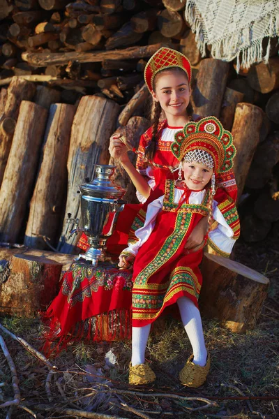 Vacker flicka i ryska folkdräkt sitter nära samovar och leende — Stockfoto