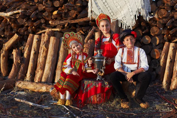 Трое очаровательных детей в народных русских костюмах и головных уборах с самоваром и в старинных туфлях — стоковое фото