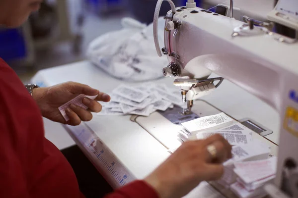 Worker on factory sewing on made in and brand name tags to produced cloths.