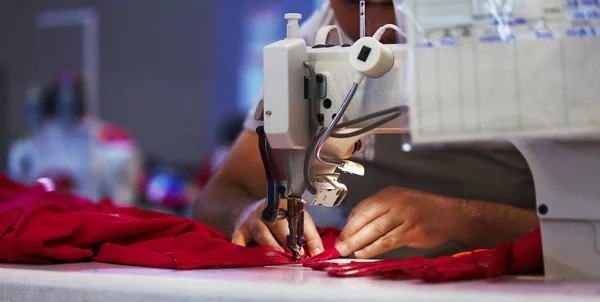 Worker or factory sewing red cloth on sewing machine