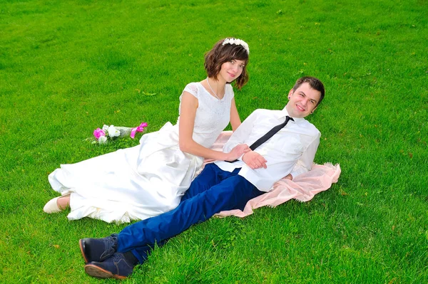 年轻、 英俊的新婚夫妇躺在绿色的草坪上 — 图库照片