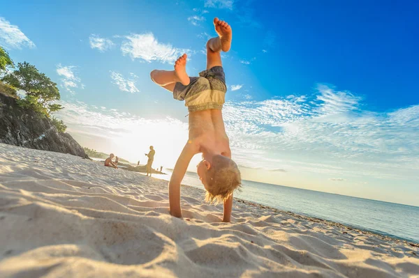 Knappe jongen van acht jaar op strand voert acrobatische schetsen een — Stockfoto