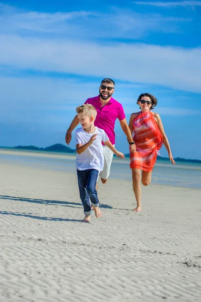 Familia de tres corriendo a lo largo de la playa tropical, riendo y —  Fotos de Stock