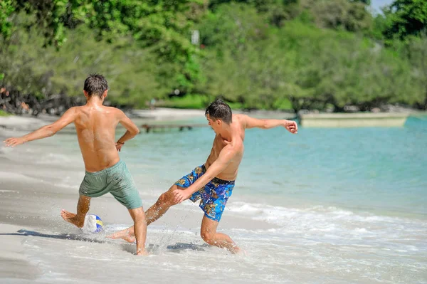 Amici che giocano a calcio sulla soleggiata spiaggia tropicale — Foto Stock