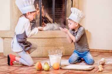 İki kardeş, erkek ve kız, şöminenin yanında şef şapkası takıyorlar. 