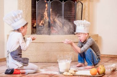 İki kardeş, erkek ve kız, şöminenin yanında şef şapkası takıyorlar. 