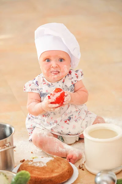 Söt liitle flicka i kock hatt sitter på kök golv smutsa — Stockfoto