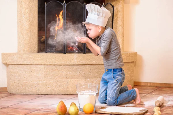 Un niño con sombreros de chef cerca de la chimenea sentado en la cocina f — Foto de Stock