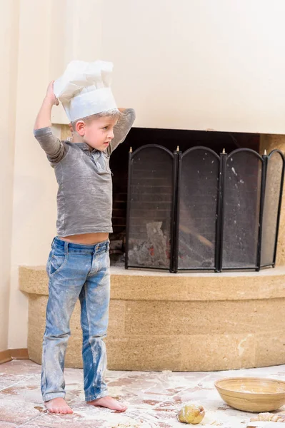 Un niño con sombreros de chef cerca de la chimenea de pie en la cocina — Foto de Stock