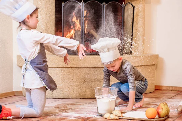 Dos hermanos - niño y niña - en sombreros de chef cerca de la chimenea — Foto de Stock