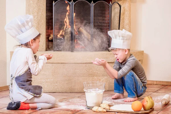 İki kardeş, erkek ve kız, şöminenin yanında şef şapkası takıyorlar. 
