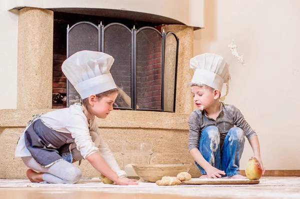 Dos hermanos - niño y niña - en sombreros de chef cerca de la chimenea — Foto de Stock