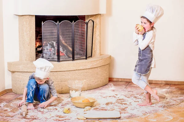 İki kardeş, erkek ve kız, şöminenin yanında şef şapkası takıyorlar. 