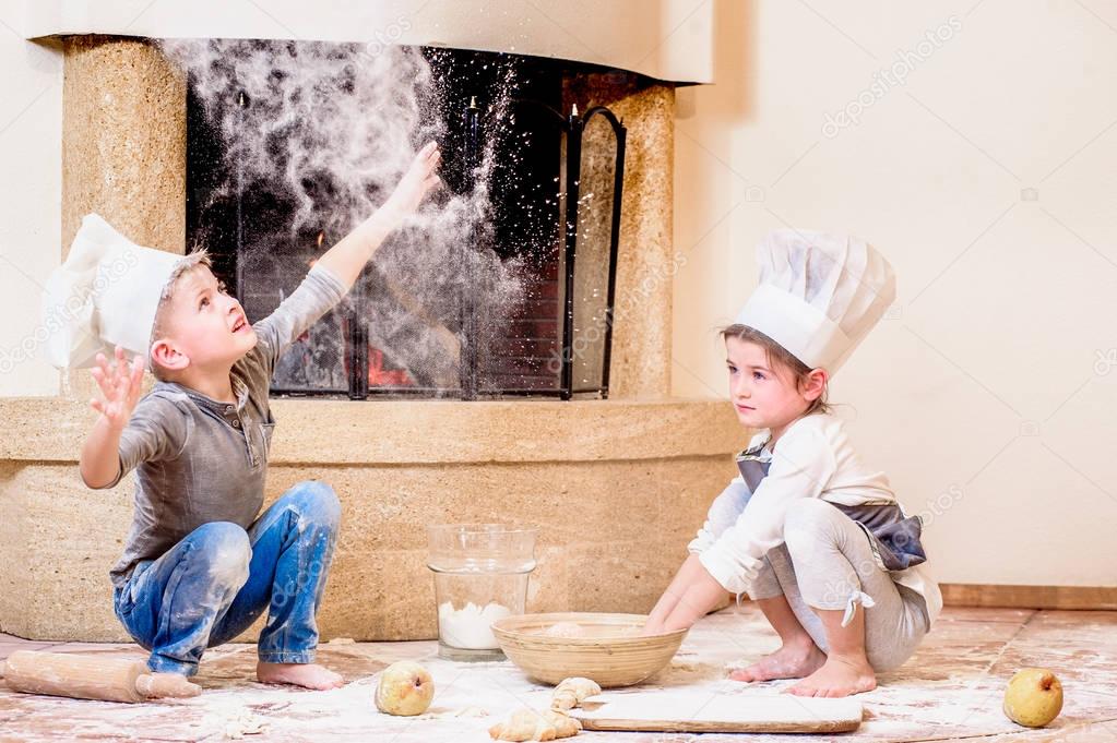 Two siblings - boy and girl - in chef's hats near the fireplace 