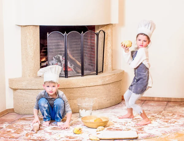Dos hermanos - niño y niña - en sombreros de chef cerca de la chimenea — Foto de Stock