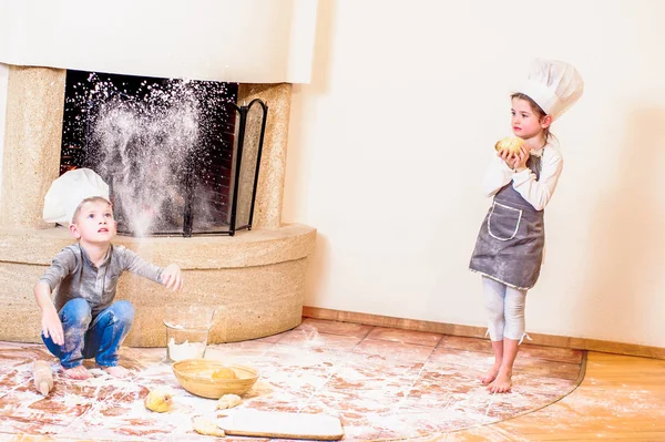 İki kardeş, erkek ve kız, şöminenin yanında şef şapkası takıyorlar. 