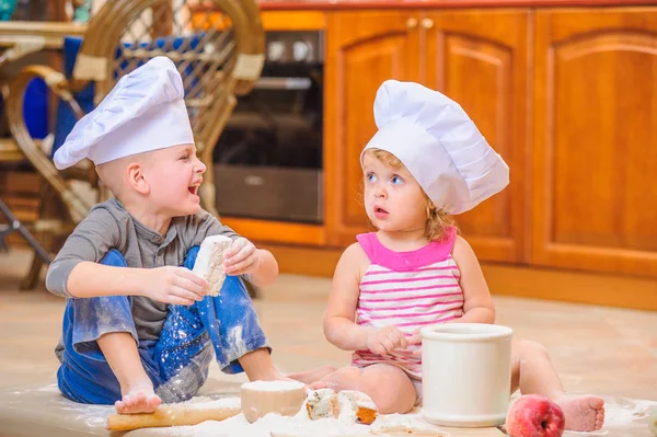 Dos hermanos - niño y niña - en sombreros de chef sentados en el kitc — Foto de Stock