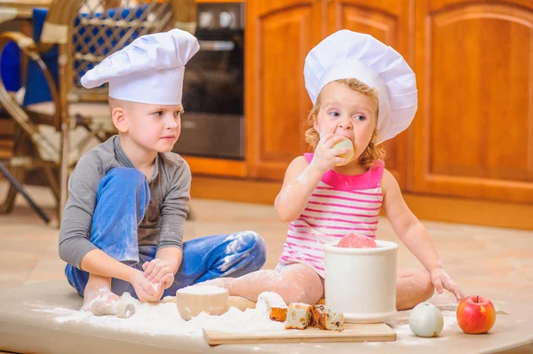 Dois irmãos - menino e menina - em chapéus de chef sentados no kitc — Fotografia de Stock