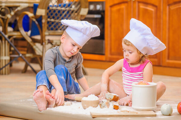 Two siblings - boy and girl - in chef's hats sitting on the kitc