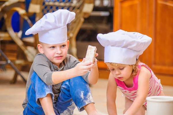 Dos hermanos - niño y niña - en sombreros de chef sentados en el kitc — Foto de Stock