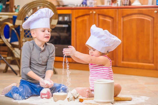 Dos hermanos - niño y niña - en sombreros de chef sentados en el kitc — Foto de Stock