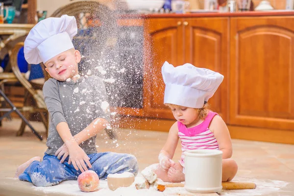 Two siblings - boy and girl - in chef's hats sitting on the kitc — Stock Photo, Image