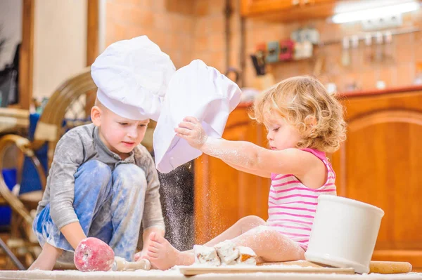 Two siblings - boy and girl - in chef 's hats sitting on the kitc — стоковое фото