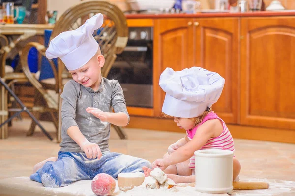 Zwei Geschwister - Junge und Mädchen - in Kochmützen auf dem Kitsch sitzend — Stockfoto