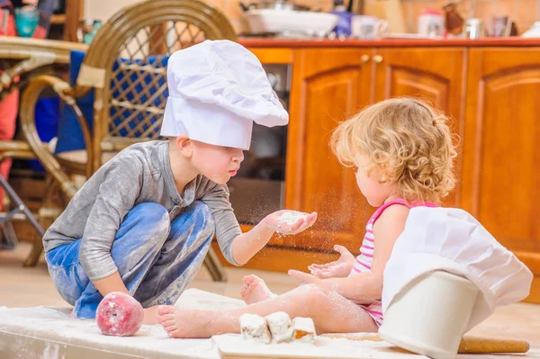 Dos hermanos - niño y niña - en sombreros de chef sentados en el kitc — Foto de Stock