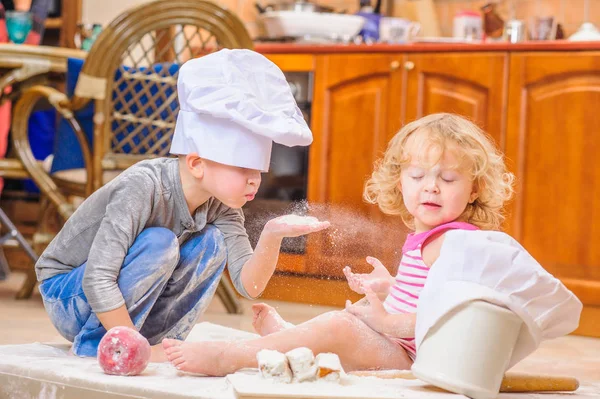 Dva sourozenci - chlapec a dívka - šéfkuchaře klobouky sedí na kuchyni. — Stock fotografie